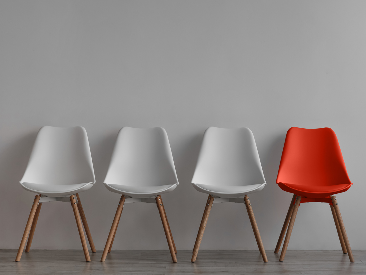 Three vacant white chairs and one red on gray wall background in office or room. Simple minimalist interior, nobody, free space. Job recruiting, leadership and business due covid-19 virus, mockup