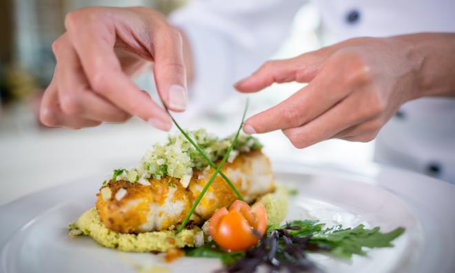 Close up on hand of a Chef decorating a beautiful plate at a fancy restaurant