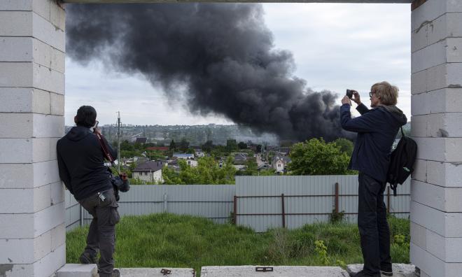 Utländska journalister betraktar på avstånd rök som stiger efter en rysk attack mot staden Charkiv i fredags. Ryska styrkor säger sig avancera i gränsorter lite längre österut. Arkivbild.