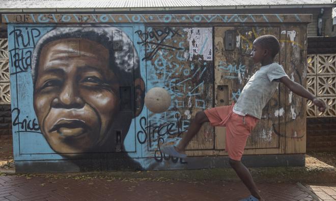 En pojke sparkar boll framför en målning föreställande Nelson Mandela i Soweto. Arkivbild.