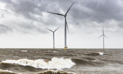 Wind turbines in an offshore wind park during a storm with big waves hitting the shore.