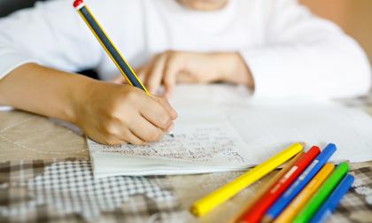 Child doing homework and writing story essay. Elementary or primary school class. Closeup of hands and colorful pencils.