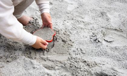 A little girl playing in the sand in the sandbox on the playground.