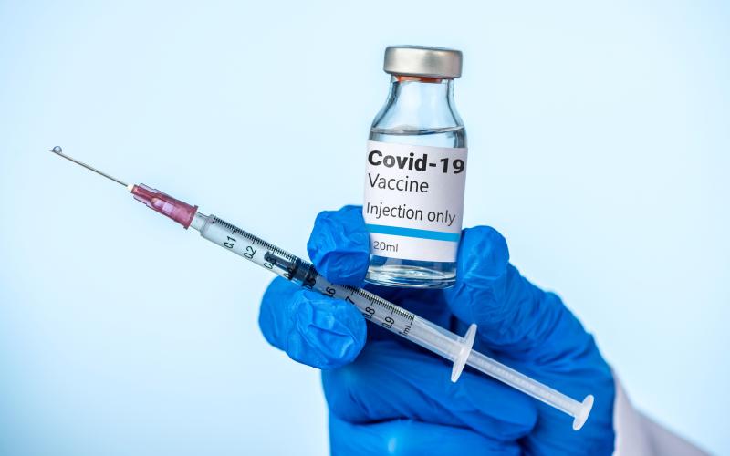 Doctor or nurse is holding the Covid-19 vaccine and syringe with her blue glove.