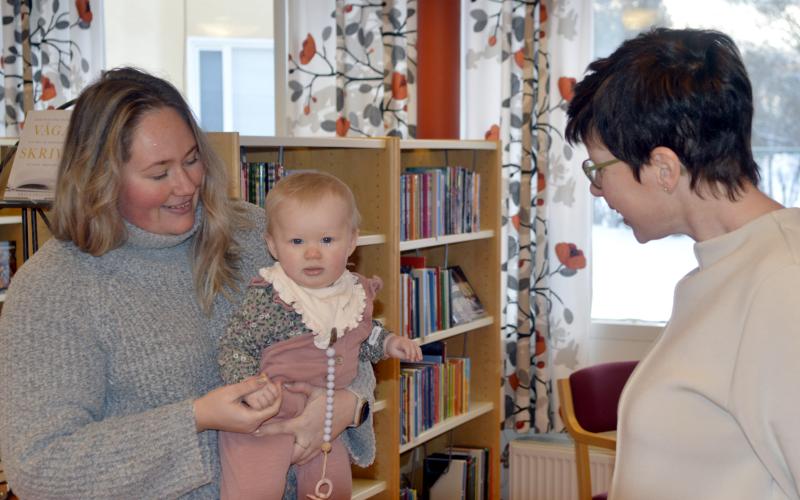 Frida Söderback och Molly Söderback hälsas välkomna till biblioteket av Sofi Ekholm som leder bebisbibban.