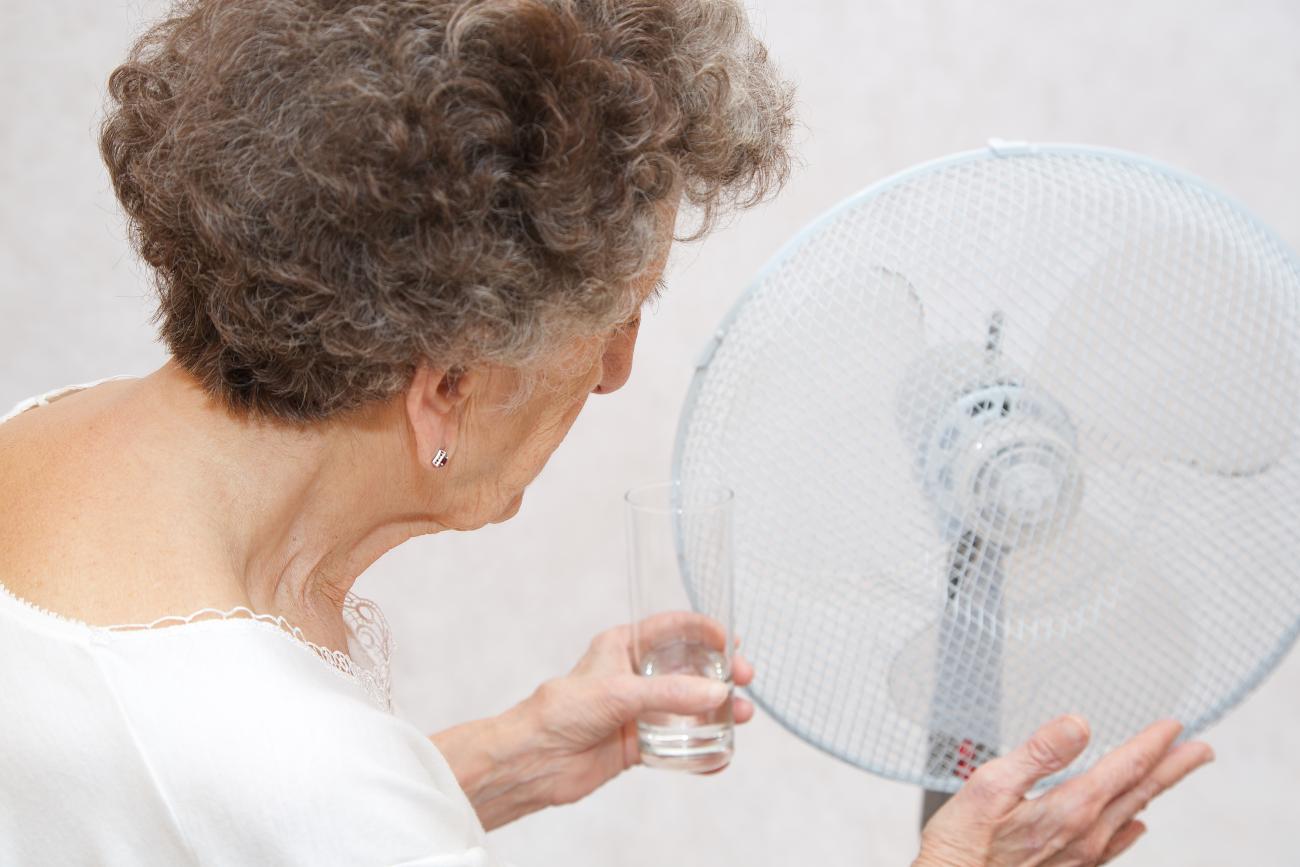 Senior woman between 70 and 80 years old stays close to the ventilator. Suffers from the heat