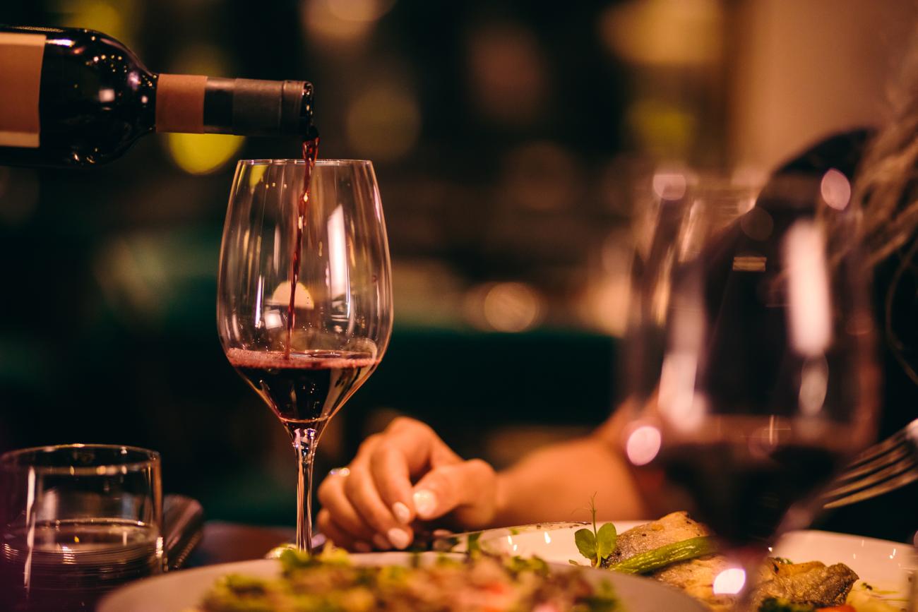 Close-up of waiter holding bottle and serving red wine during dinner at luxurious gourmet restaurant