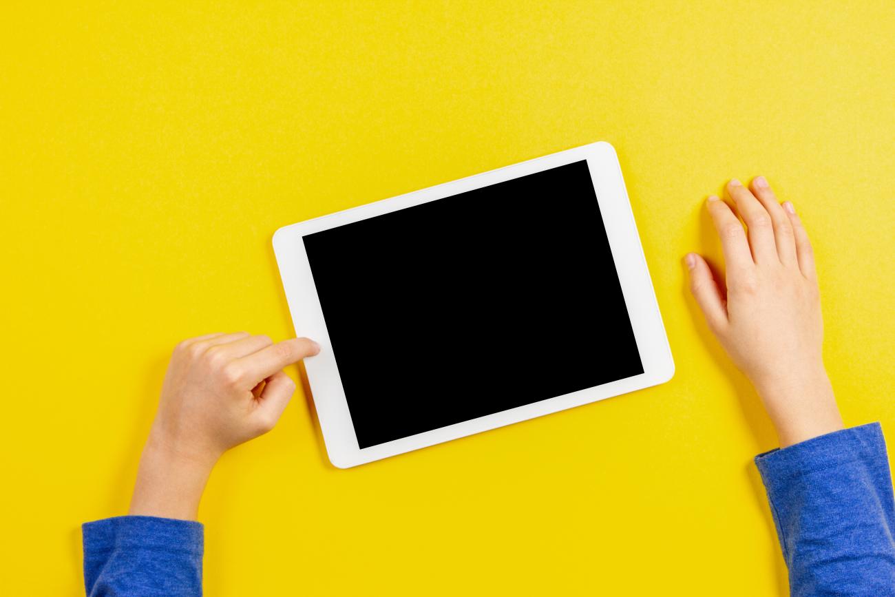 Kid hands with tablet computer on yellow background.