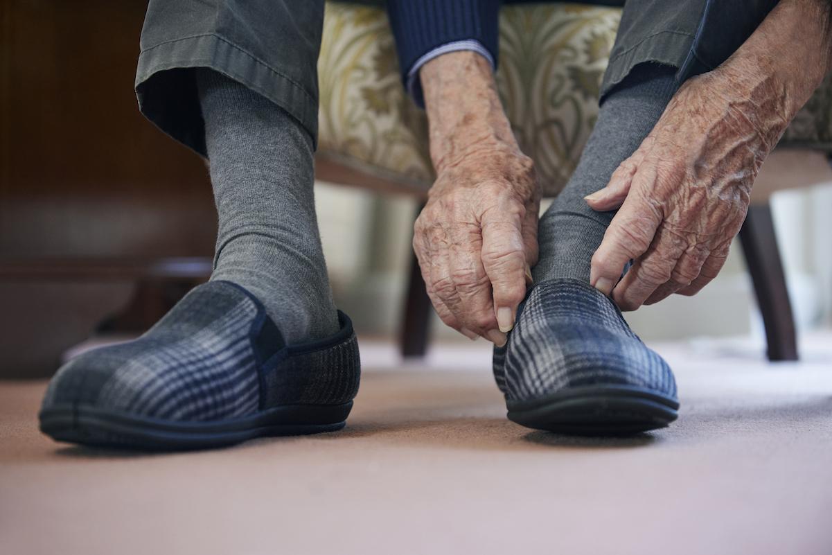 Close Up Of Senior Man Putting On Slippers To Keep Feet Warm In Cost Of Living Crisis